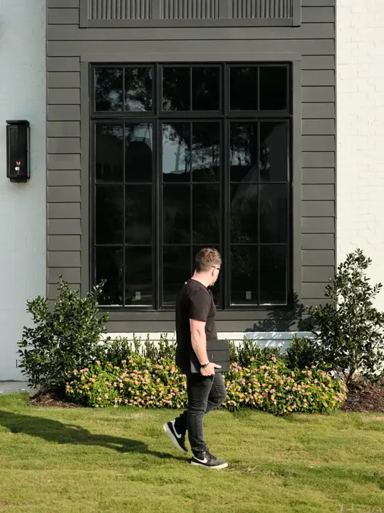 Team member walking past shrub and flower beds beside a gray home