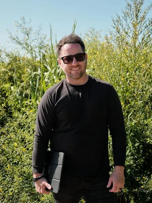Team member standing among tall grasses with a tablet