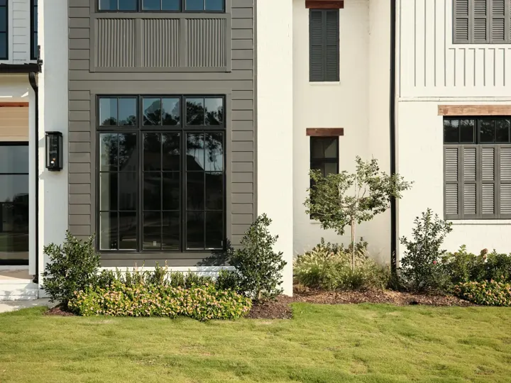 White home exterior with black framed windows, a trimmed lawn and planted beds