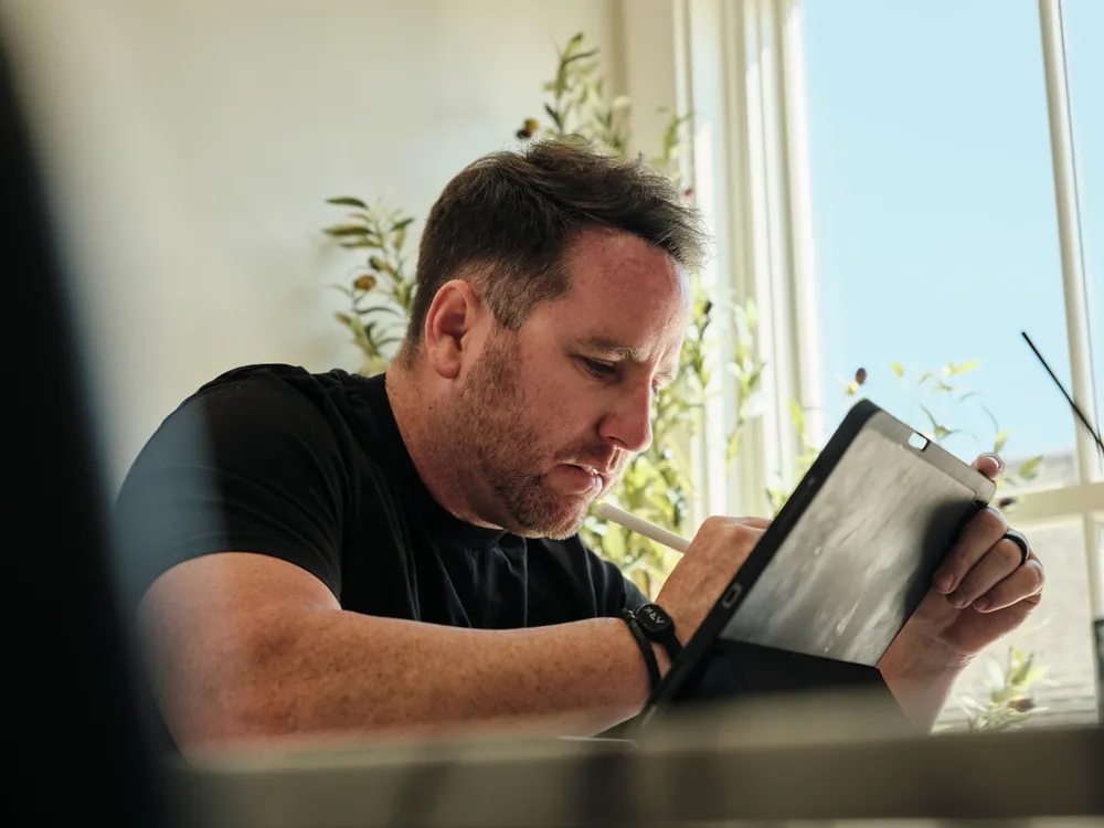 Team member sketching a design on a tablet by a bright window