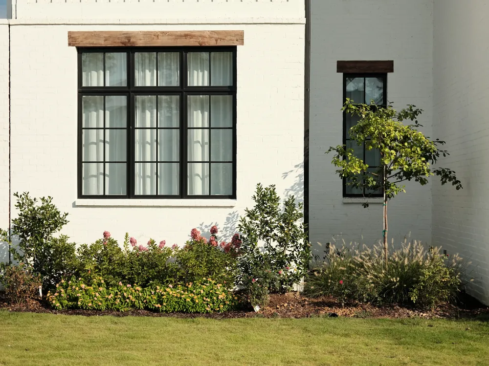 White house with black windows above landscaped beds and a lawn