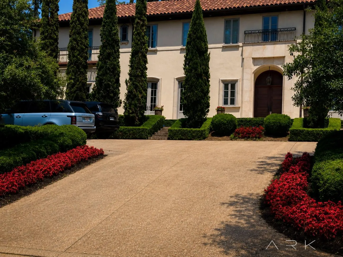 Stone driveway between clipped hedges and red flower beds at a large home