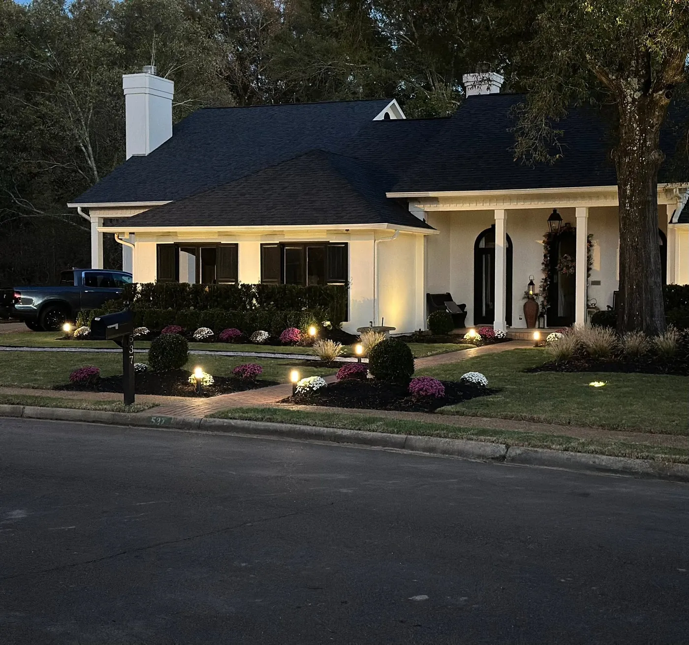 Home lit at dusk with landscape lighting over its lawn and shrub beds