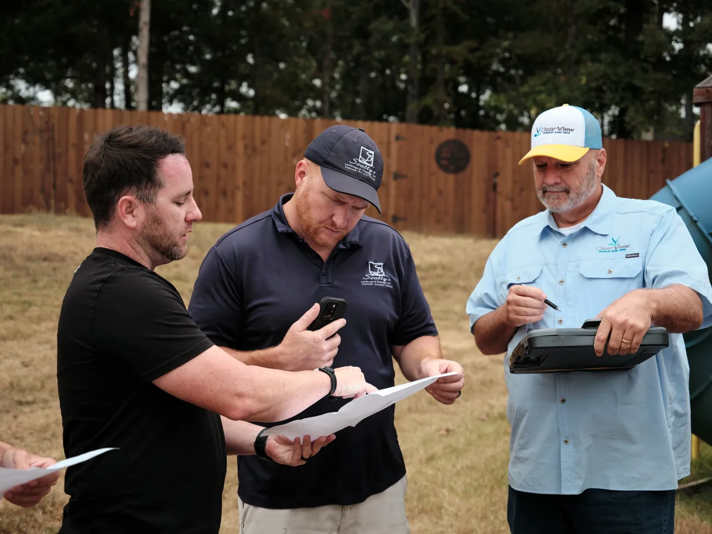Three men reviewing plans together in a backyard